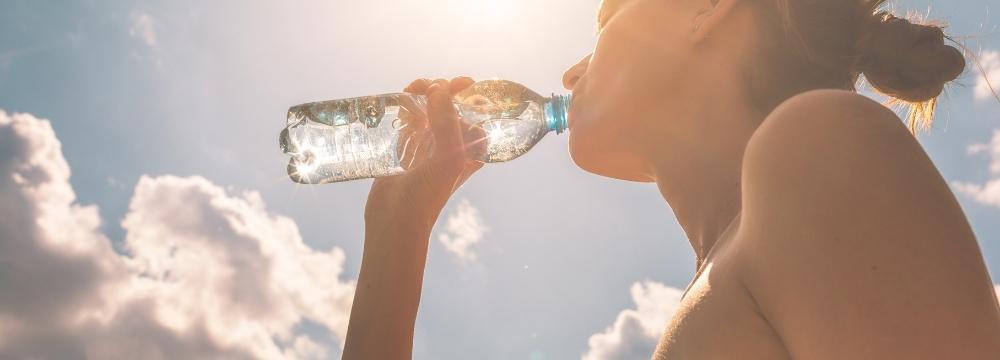 Woman drinking out of clear plastic water bottle while sun shines in her face