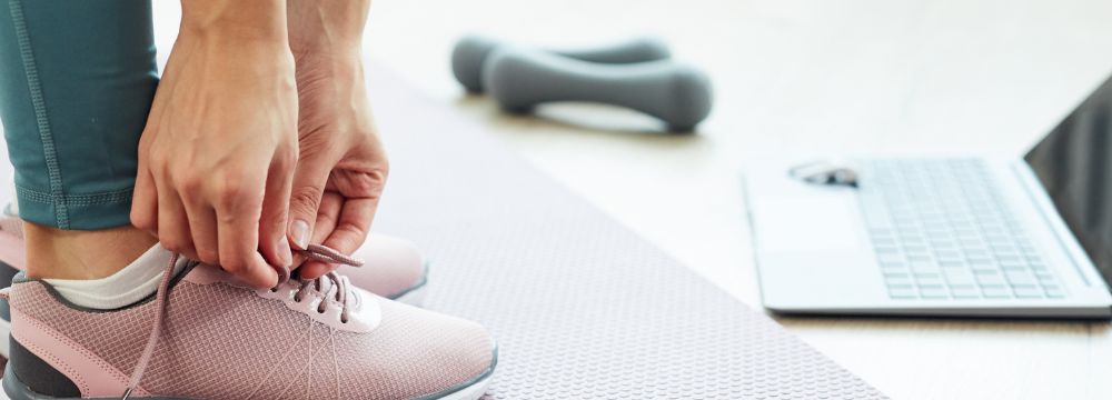 Woman tying shoes in front of dumbbells and laptop preparing to exercise