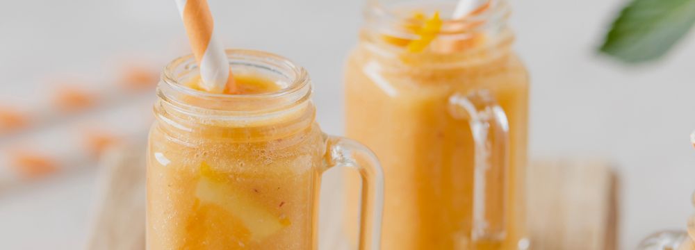 two orange smoothies in mason jars on counter