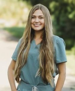 Nurse in blue scrubs smiling outside